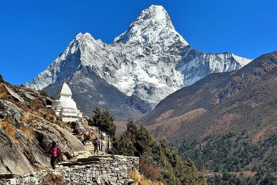 Trekker passing white Buddhist stupa with Ama Dablam mountain peak behind